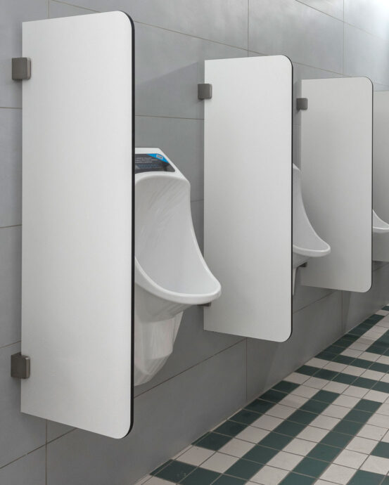 Novosan Urimat-pisuaarit ja Ujo-väliseinät kuvattuna sivusta miesten WC:ssä. Valkoiset pisuaarit ja väliseinät on asennettu miesten WC:n seinään. Seinässä on harmaa vaaka laatoitus. Lattiassa on tummanvihreää ja valkoista lattialaattaa.