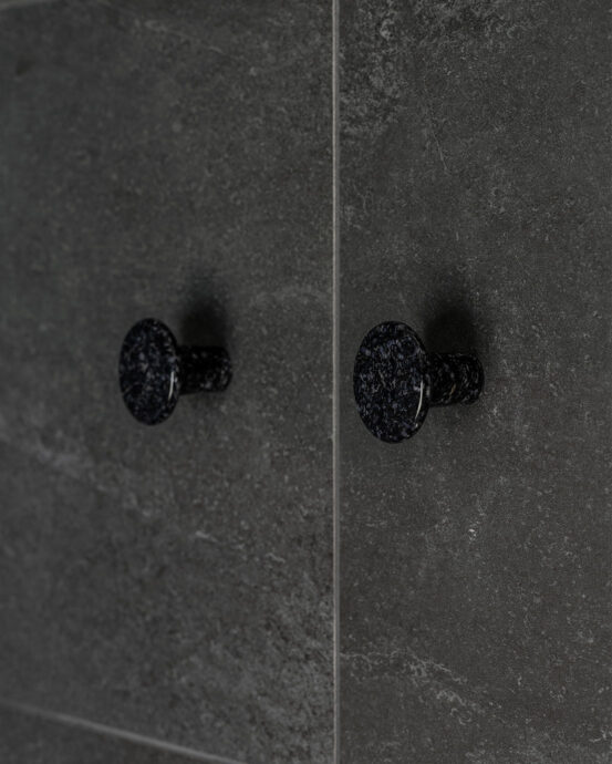 Woodio Hook -vaatekoukut. Kaksi pyöreää hiilenmustaa vaatekoukkua kuvattuna tummassa seinässä. Tuotenumero: 6438441029375.