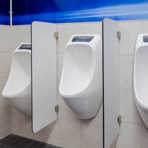 Kolme vedetöntä, valkoista urinaalia on kiinnitetty miesten vessan seinään. Urinaalit on asennettu eri korkeuksille. Urinaalien kaksi väliseinää ovat vaaleat ja eri korkeu.