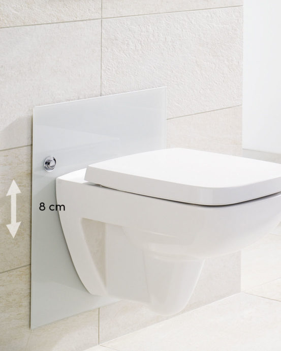 Vaaleassa WC-tilassa on korkeussäädettävä valkoinen seinä-WC-istuin, seinässä lasinen peitelevy ja huuhtelunappi.