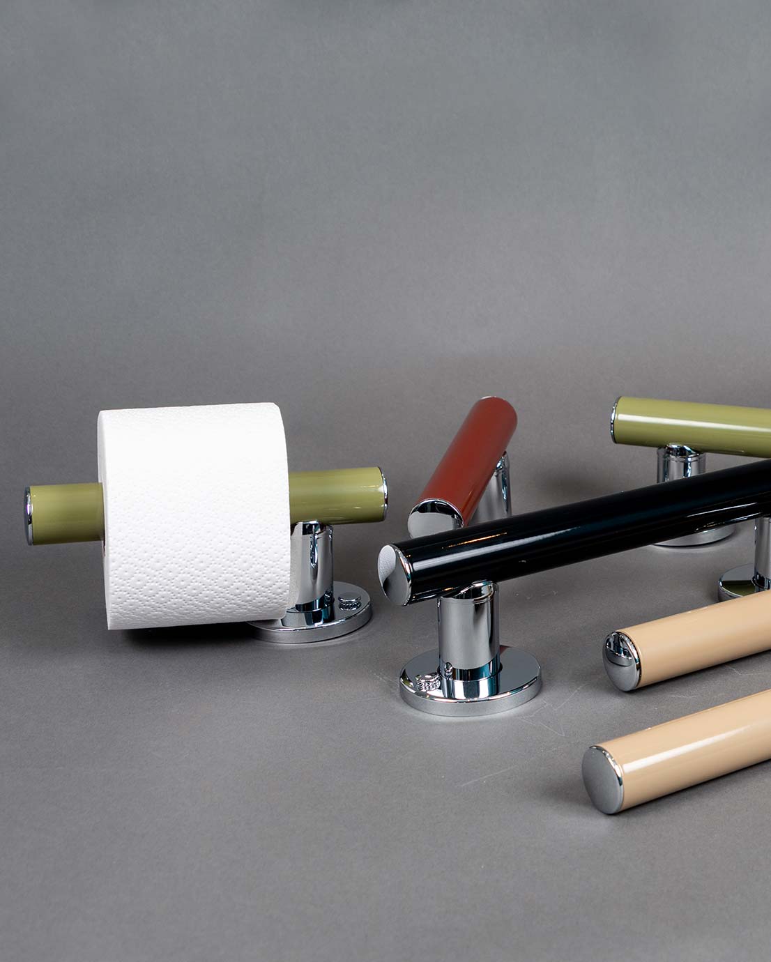 Väggmonterade stödhandtag på grå bakgrund, 5 st. Färger: grön, svart och beige. Modeller: rakt stödhandtag, stödhandtag/toalettpappershållare, stödhandtag för toalettstol samt böjt stödhandtag av V-modell..