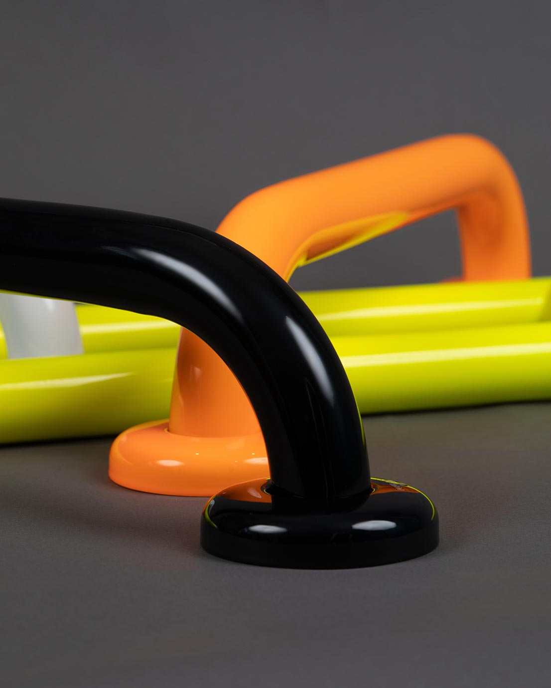 Tukikahvat harmaalla taustalla. Värit: edessä, musta. Takana oranssi ja keltainen (huomiovärit).