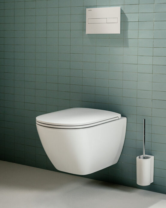 Vägghängd Laufen Lua-toalettstol med lock på en grön kakelvägg. Bilden visar även en vit spolknapp och en vägghängd, vit toalettborste. Produktnummer:  H8200804000001, H8200834000001, H8910830180001. Färg: vit.