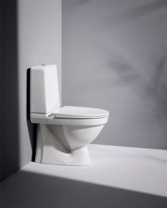 Bilden visar en vit Laufen Kompas-toalettstol sedd från sidan. Toalettutrymmet har väggar och golv i grått..