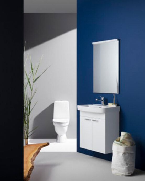 Bilden visar en vit Laufen Kompas-toalettstol. I toalettrummet sitter även en vit handfatskommod och en spegel på en blå vägg.