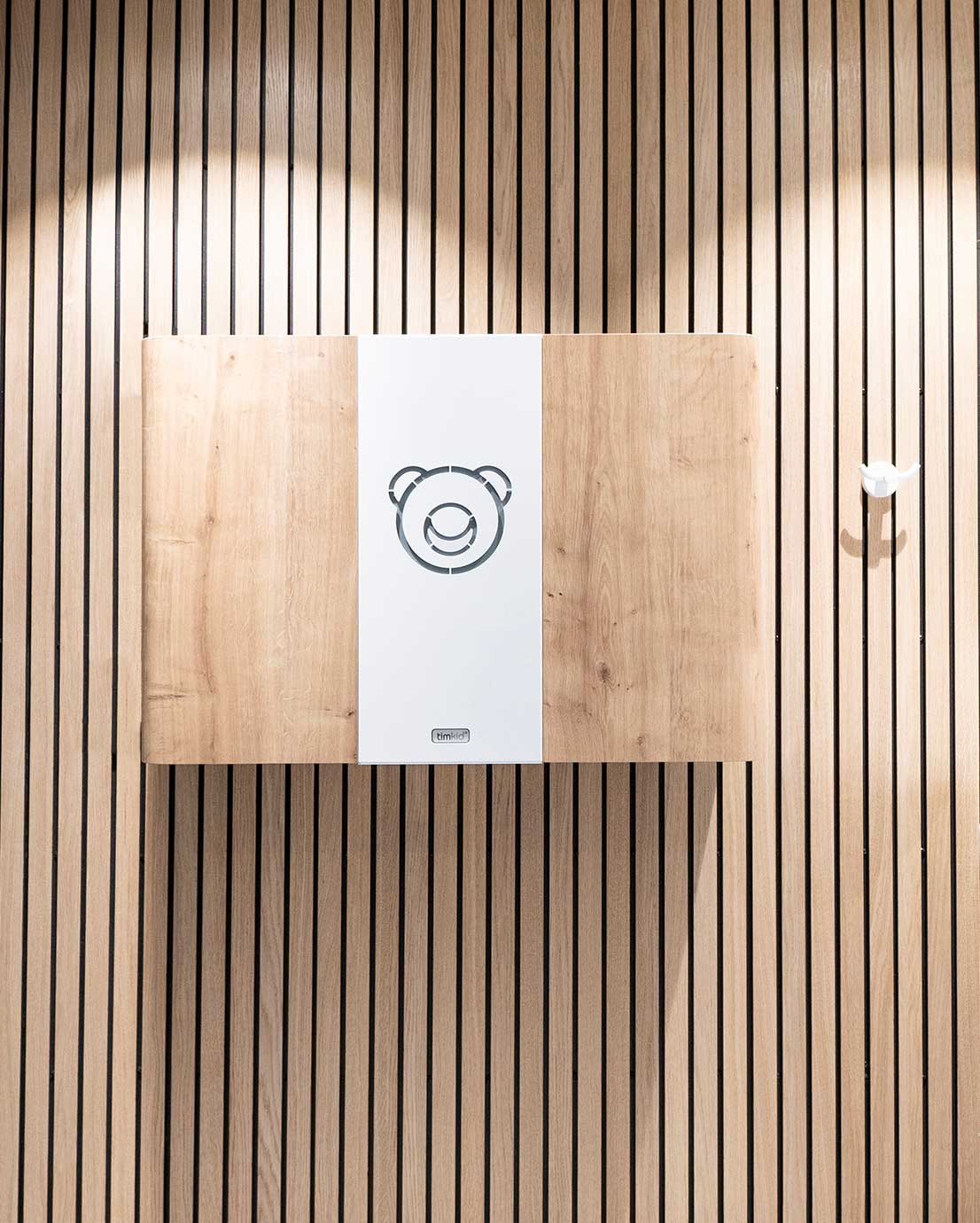 Puiseen rimapaneeliseinään on kiinnitetty Timkid-lastenhoitopöytä ja valkoinen vaatekoukku. Lastenhoitopöydän väri: tammi. Malli: KAWAQ.